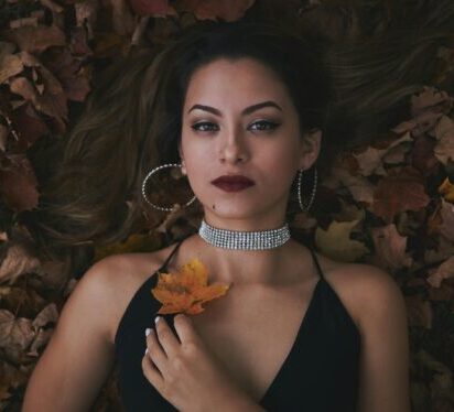 A woman in elegant fashion lies on autumn leaves, showcasing jewelry and style.