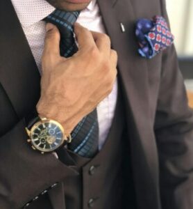 Elegant close-up of a man in a designer suit adjusting his tie, showcasing luxury fashion.